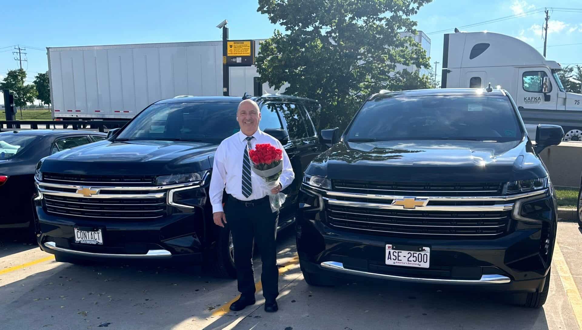 Contact Limo chauffeur welcoming passengers beside two luxury SUVs